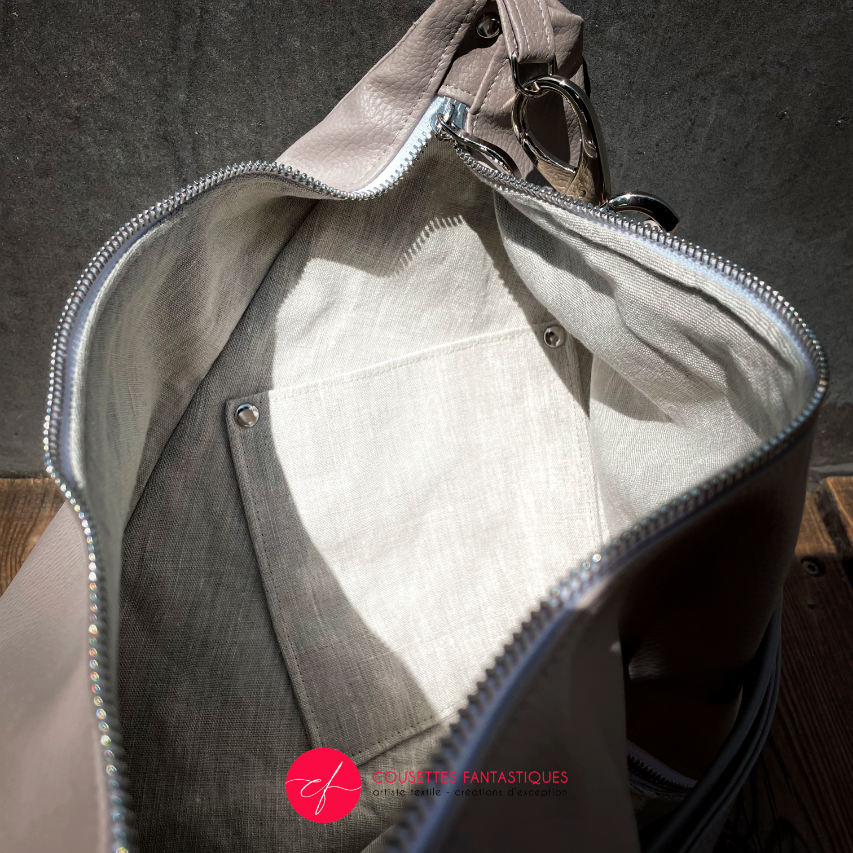 A triangular shoulder bag made of beige synthetic leather and white, cream, beige, and green babywearing fabric.