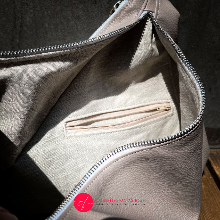 A triangular shoulder bag made of beige synthetic leather and white, cream, beige, and green babywearing fabric.