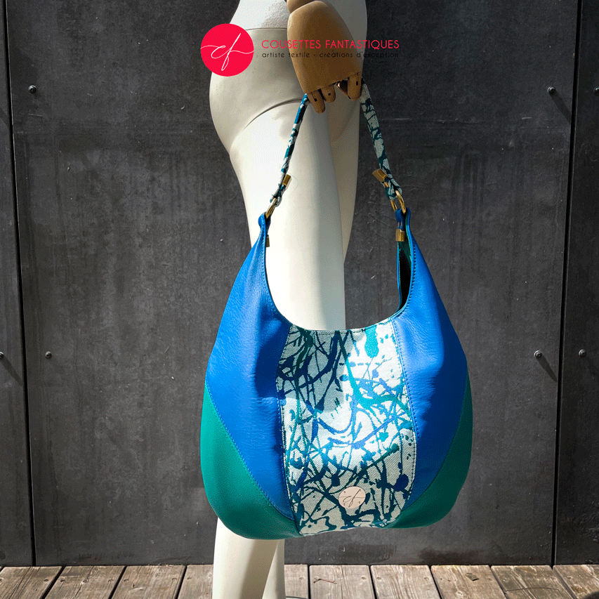 A shoulder bag made of royal blue and sage green leather, white, blue, and green babywearing fabric with an organic pattern, and fir green poplin.