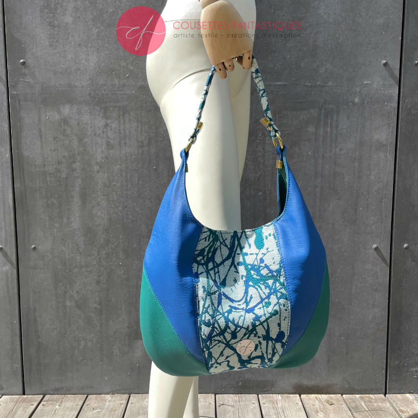 A shoulder bag made of royal blue and sage green leather, white, blue, and green babywearing fabric with an organic pattern, and fir green poplin.