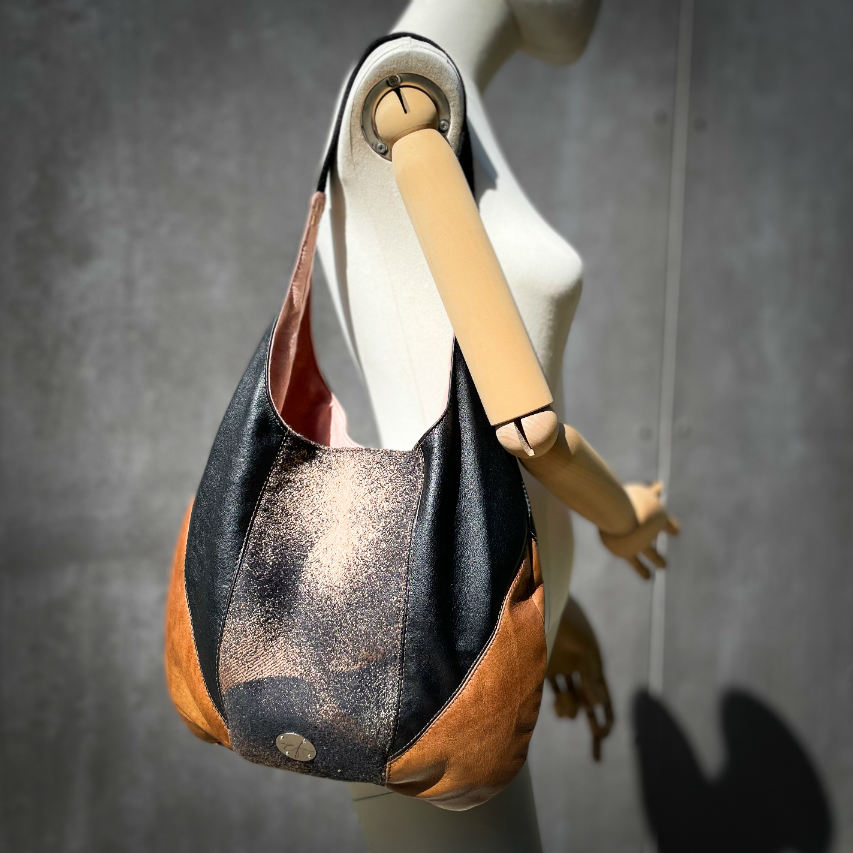 A shoulder bag made of brown and black leathers, a black, brown, and beige babywearing wrap with a round abstract pattern, and peach linen canvas.