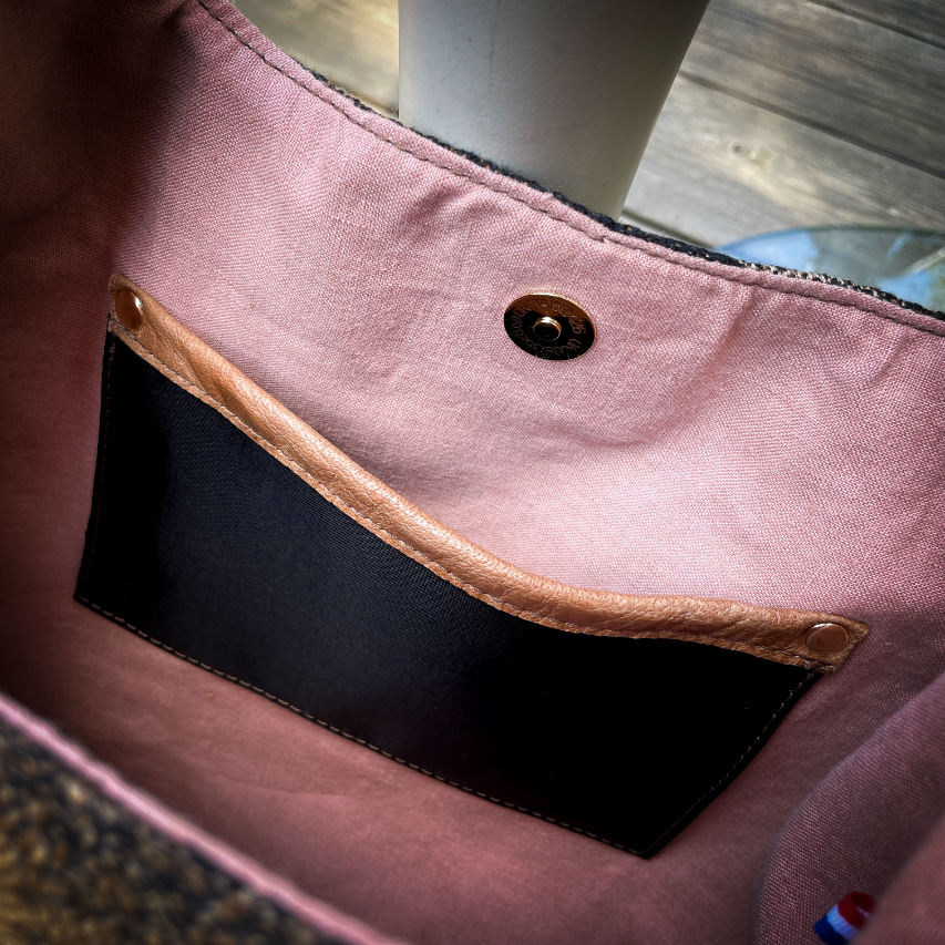 A shoulder bag made of brown and black leathers, a black, brown, and beige babywearing wrap with a round abstract pattern, and peach linen canvas.