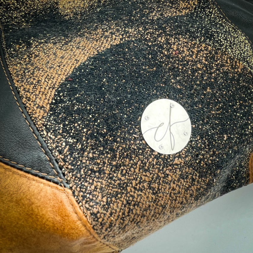 A shoulder bag made of brown and black leathers, a black, brown, and beige babywearing wrap with a round abstract pattern, and peach linen canvas.