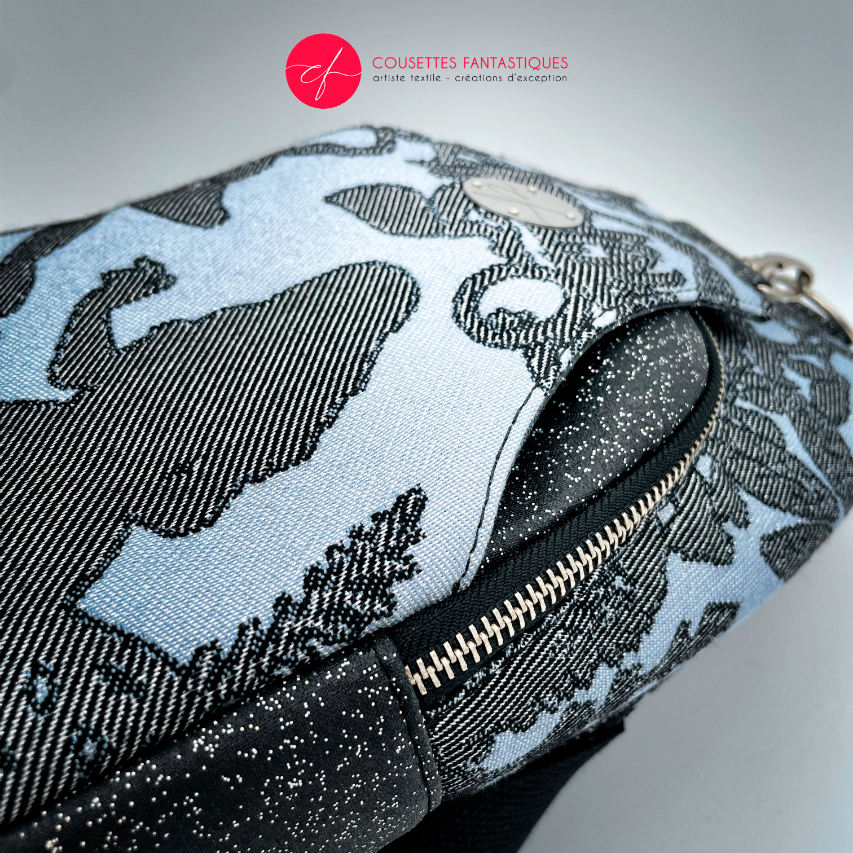 A backpack made from multicolored glitter canvas and a gray-blue, black, and silver-glitter woven wrap with a motif inspired by the Alice in Wonderland story.