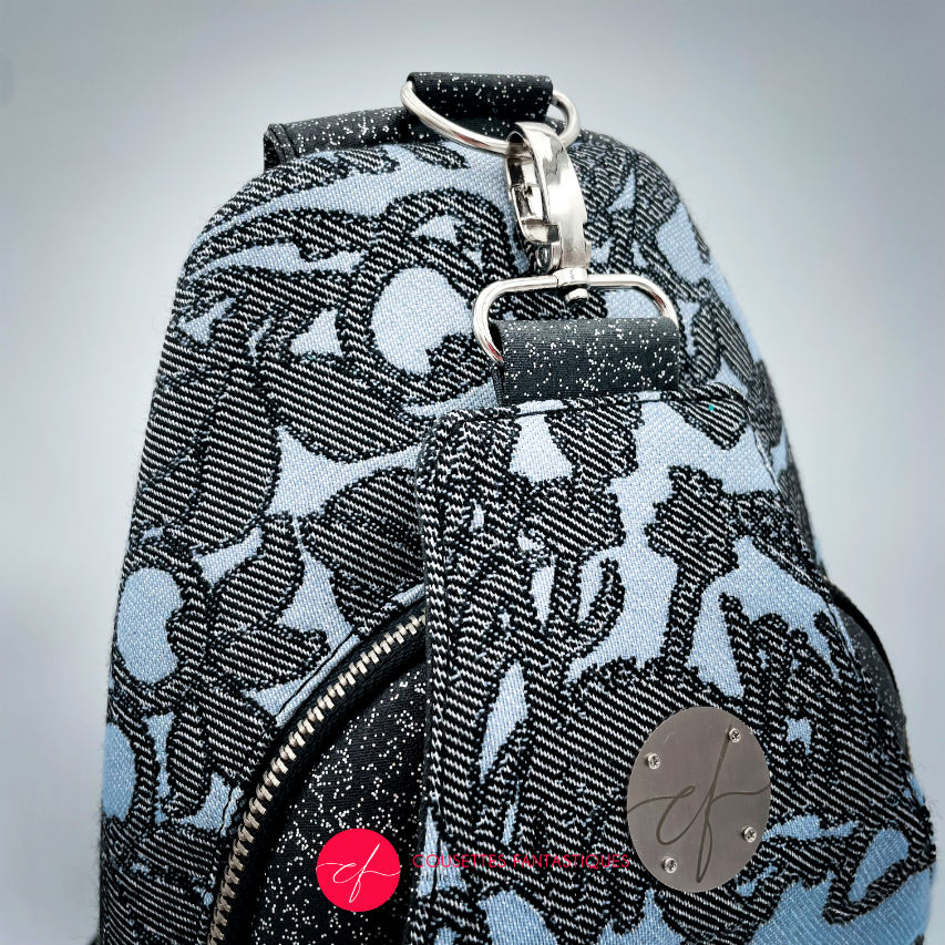 A backpack made from multicolored glitter canvas and a gray-blue, black, and silver-glitter woven wrap with a motif inspired by the Alice in Wonderland story.