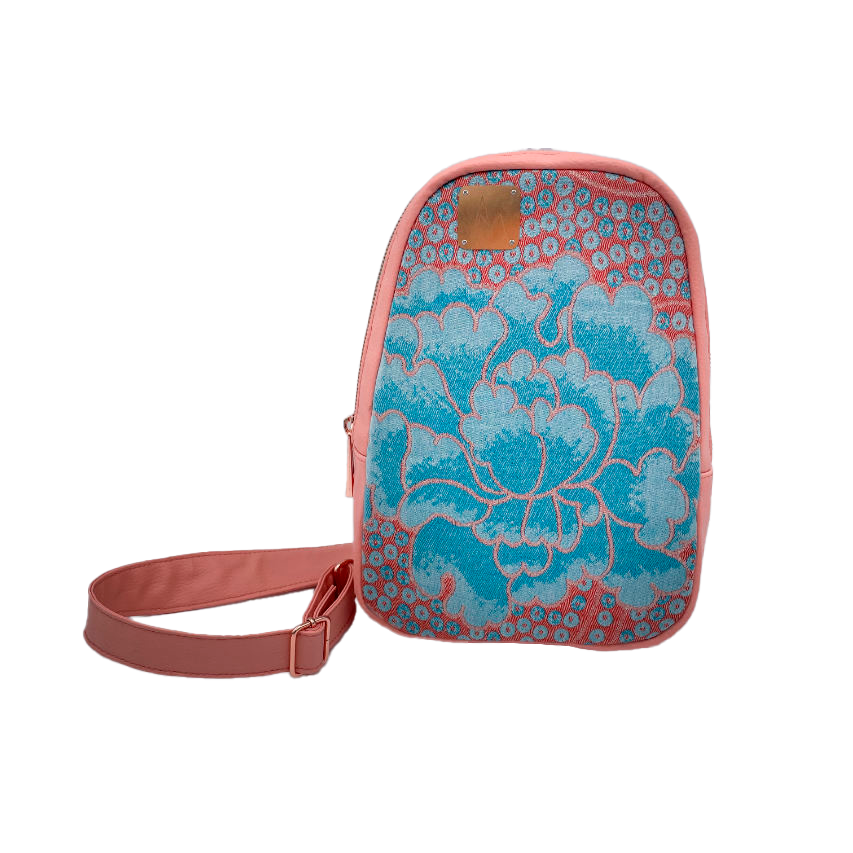 A backpack made of peach-colored faux leather and a babywearing wrap in shades of pink and turquoise with a vintage floral pattern.