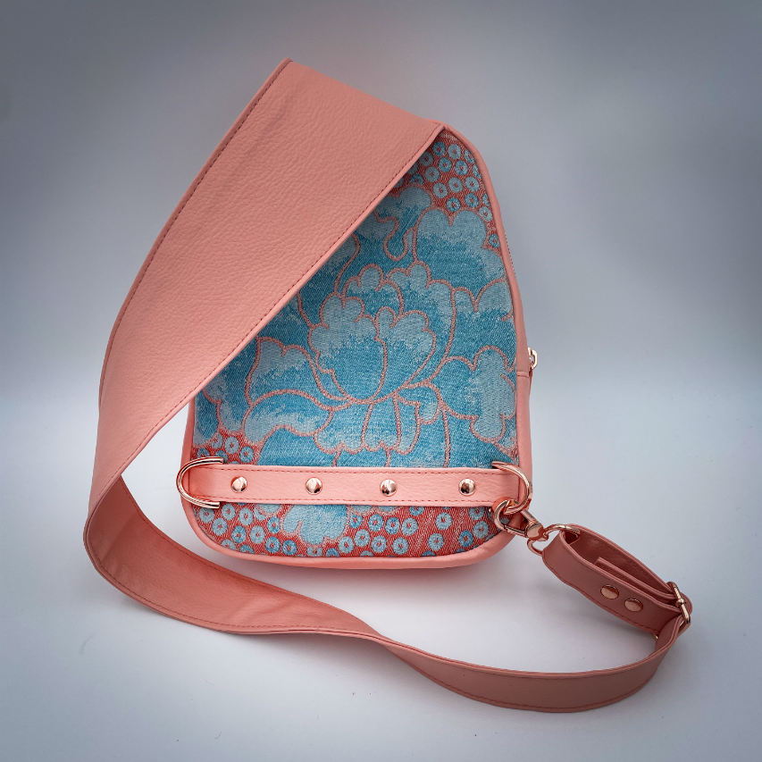 A backpack made of peach-colored faux leather and a babywearing wrap in shades of pink and turquoise with a vintage floral pattern.