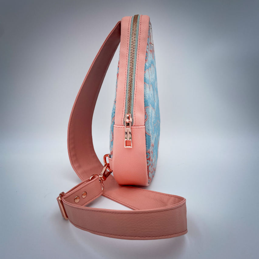 A backpack made of peach-colored faux leather and a babywearing wrap in shades of pink and turquoise with a vintage floral pattern.