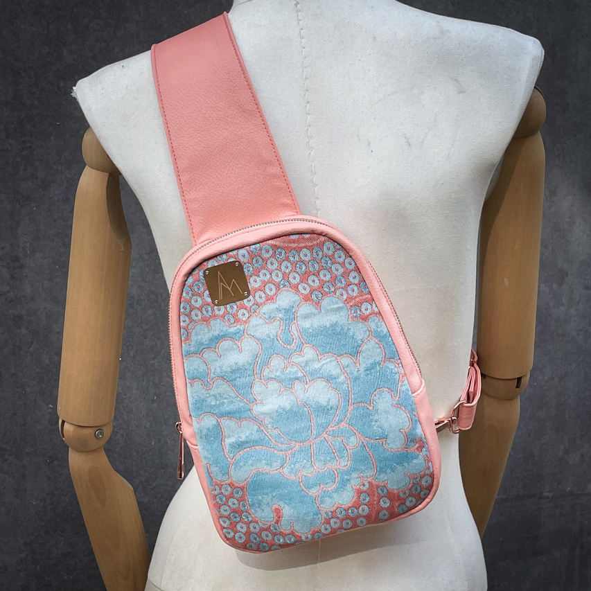 A backpack made of peach-colored faux leather and a babywearing wrap in shades of pink and turquoise with a vintage floral pattern.