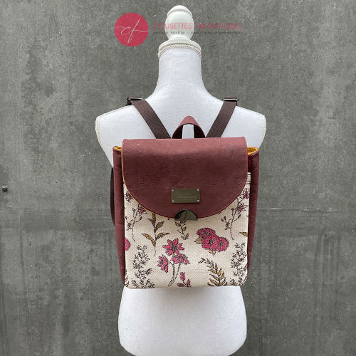 A backpack made with scarf fabric in floral patterns in pink tones on ecru background and brick cork.