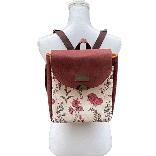 A backpack made with scarf fabric in floral patterns in pink tones on ecru background and brick cork.