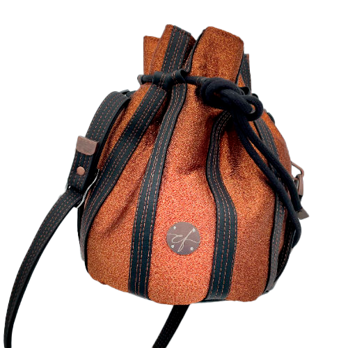 A shiny “bucket” bag made with shiny bronze fabric outlined by butter smooth matte black faux leather.