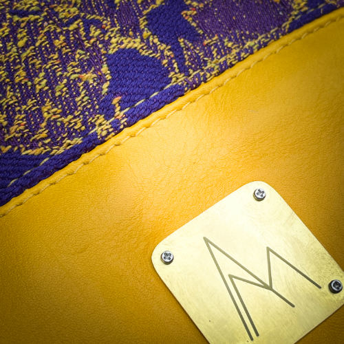 A bucket bag made from babywearing wrap fabric featuring yellow thistles on a purple background with yellow lamb leather.