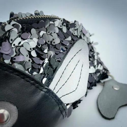 A zippered pouch sewn with black faux leather, black and white sequined fabric, and gray denim.