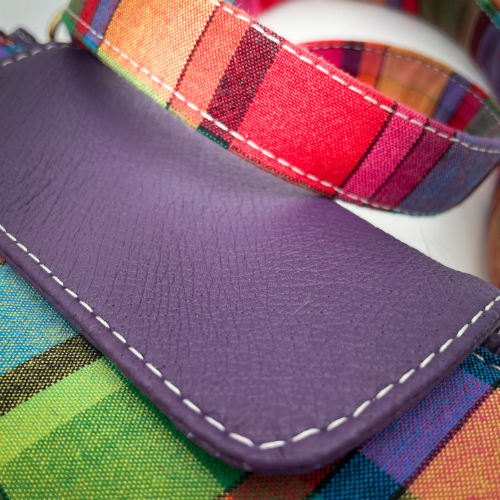 A hybrid clutch wallet bag made of purple leather and multicolored madras fabric.