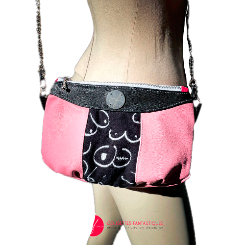 A messenger bag made from a black and white babywearing wrap with stylized breast drawings, black stingray leather, and pink stingray leather.