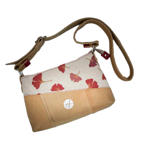 A rectangular crossbody bag made from camel colored leather and a red Ginkgo Biloba leaves patterned polycotton canvas.