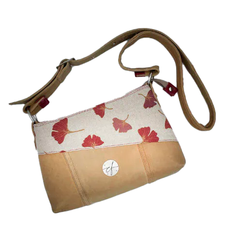 A rectangular crossbody bag made from camel colored leather and a red Ginkgo Biloba leaves patterned polycotton canvas.