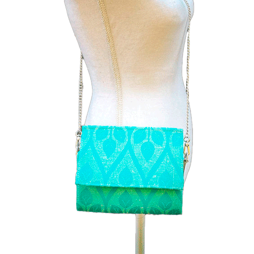 A flat handbag with a flap made from cream and turquoise babywearing wrap with stylized leaf pattern.