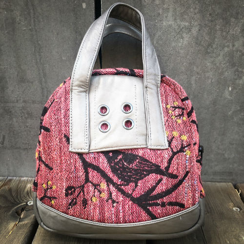 A mini handbag made of babywearing wrap scraps showing birds in a tree in pink and black tones, and grey lambskin leather.