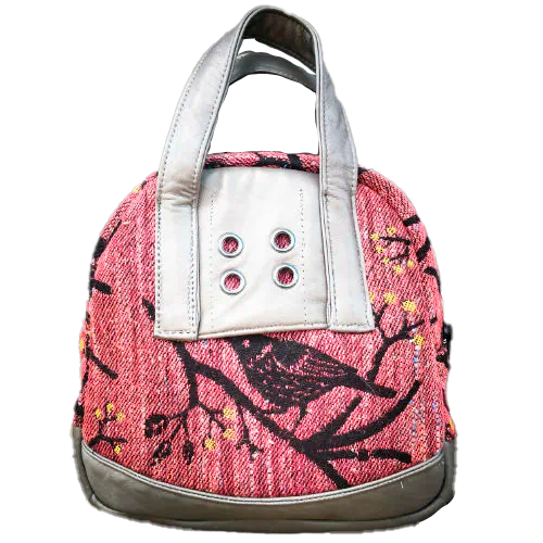 A mini handbag made of babywearing wrap scraps showing birds in a tree in pink and black tones, and grey lambskin leather.