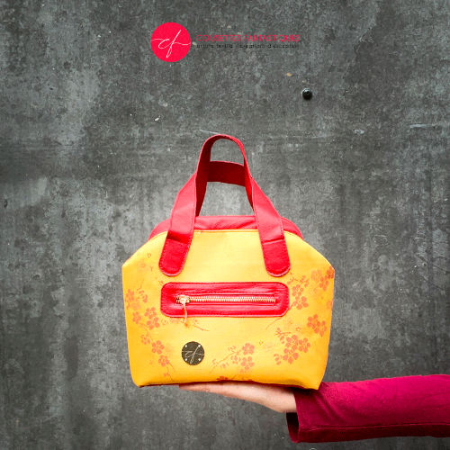 A mini handbag made of yellow upholstery fabric with a red cherry blossom pattern and red leather.