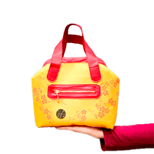 A mini handbag made of yellow upholstery fabric with a red cherry blossom pattern and red leather.