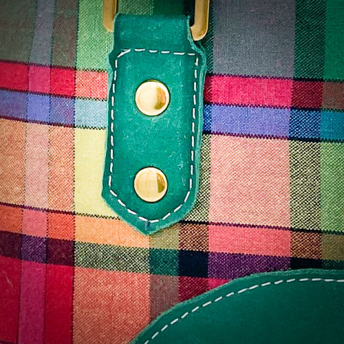 A wallet bag made of forest green leather and multicolored madras fabric.