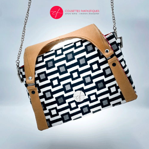 A handbag made of black and white babywearing fabric with a geometric pattern, caramel leather, and red poplin.