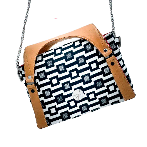 A handbag made of black and white babywearing fabric with a geometric pattern, caramel leather, and red poplin.