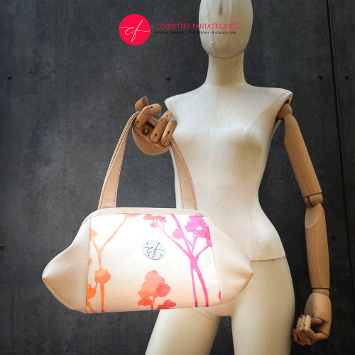A handbag made of cream synthetic upholstery fabric and cream faux leather, featuring a gradient botanical pattern from pink to orange.