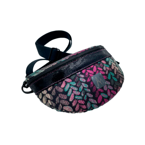 A fanny pack sewn from black patent leather and a scrap of baby wrap fabric with a pattern of green, beige, and pink stitches on a black background, paired with bright pink poplin lining inside.