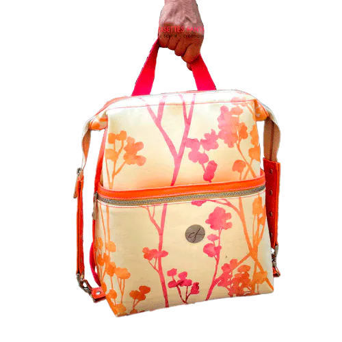 A backpack made with bright orange synthetic leather and cream upholstery fabric with a gradient of plant patterns from pink to orange.
