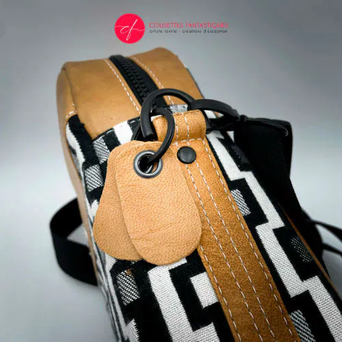 A messenger bag made from a black and white geometric pattern babywearing wrap, caramel leather, and red poplin.