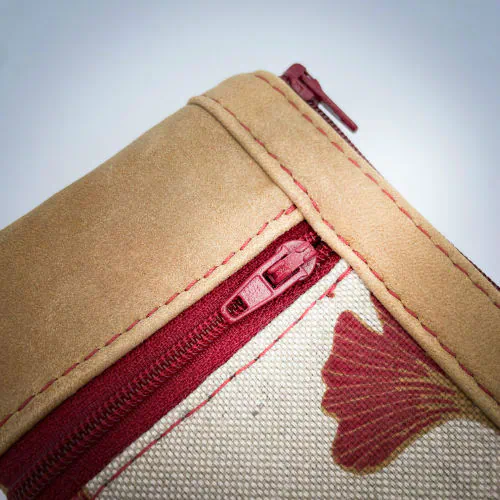 A mini zippered coin purse made of camel colored leather and a red Ginkgo Biloba leaves patterned polycotton canvas.