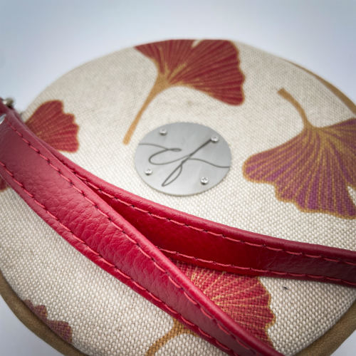 A round pouch made of camel colored leather and a red Ginkgo Biloba leaves patterned polycotton canvas.