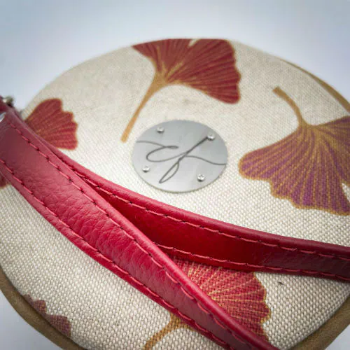 A round pouch made of camel colored leather and a red Ginkgo Biloba leaves patterned polycotton canvas.