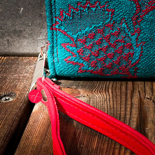 A small zippered card and coin holder made from blood-red and emerald green wrap fabric with thistle patterns and emerald green linen. It comes with a bright red faux leather wrist strap.