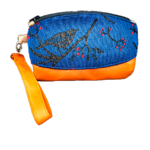A small zippered clutch sewn in orange leather and a babywearing wrap in electric blue, black, and red with a motif of birds in branches.
