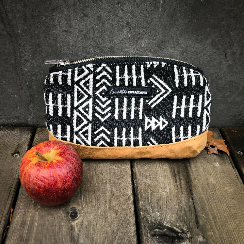 A small zippered clutch made of washable caramel paper, a black and white geometric patterned babywearing wrap, and grey poplin.