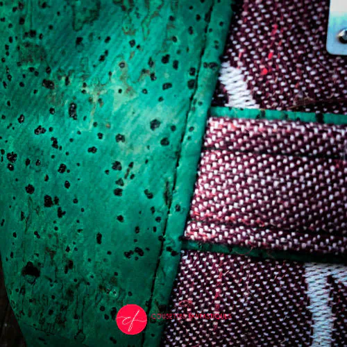 A zippered pouch sewn from a mauve and green babywearing wrap with a bird motif on branches, combined with emerald green cork.