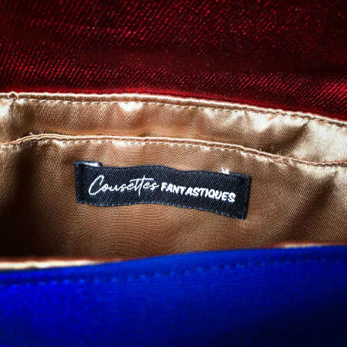 A small flap clutch sewn in blue canvas, metallic red-coated denim, and a glittery avian patterned babywearing wrap, lined with golden satin.