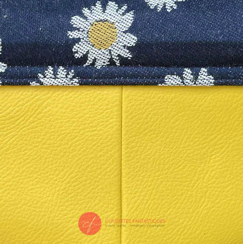 A small bag made from yellow faux leather and a fabric coupon with white and yellow daisies on a navy blue background.