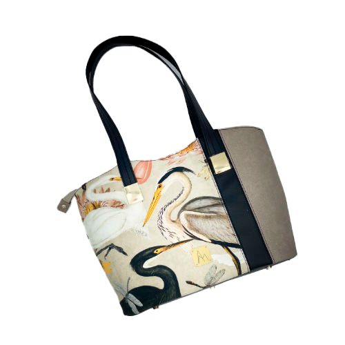 A large zippered shoulder bag, reminiscent of a tote, made from a thick fabric with a wild bird pattern, combined with black and taupe faux leather, and lined with mottled cream linen and coral.