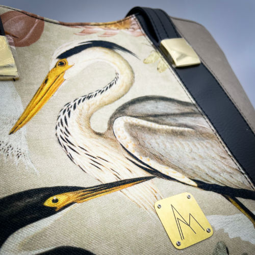 A large zippered shoulder bag, reminiscent of a tote, made from a thick fabric with a wild bird pattern, combined with black and taupe faux leather, and lined with mottled cream linen and coral.