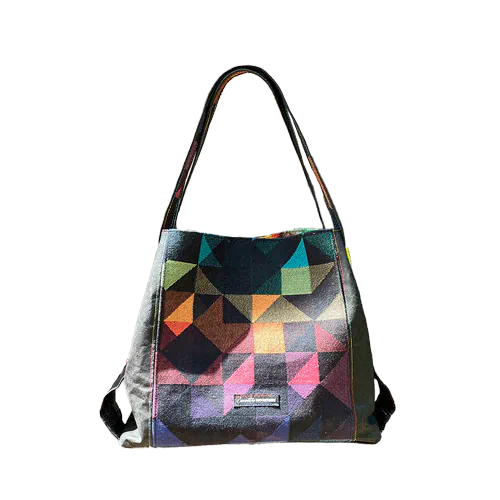 A shoulder bag made from black and rainbow geometric-patterned babywearing scarf and black cork, with a bright rainbow swirl interior.