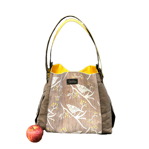 A shoulder bag made from black and rainbow geometric-patterned babywearing scarf and black cork, with a bright rainbow swirl interior.