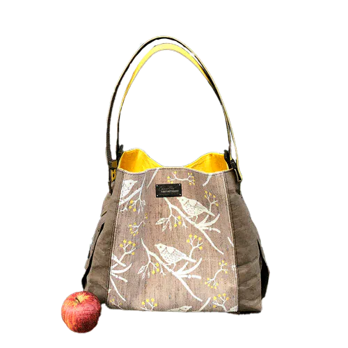 A shoulder bag made from black and rainbow geometric-patterned babywearing scarf and black cork, with a bright rainbow swirl interior.