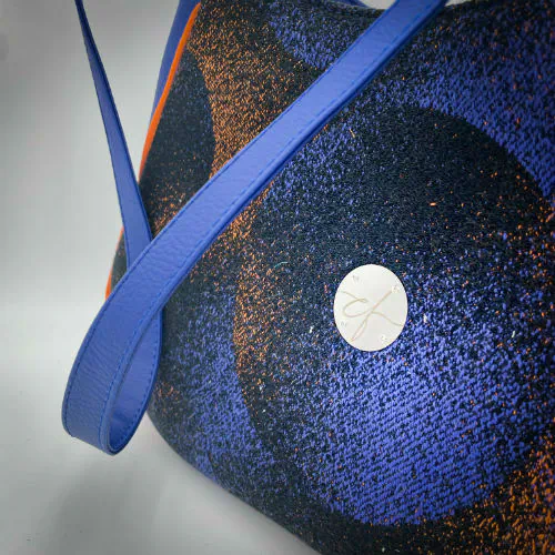 A zippered shoulder bag made from black, blue, pink and orange babywearing wrap scrap, royal blue faux leather, and bright light orange lining.