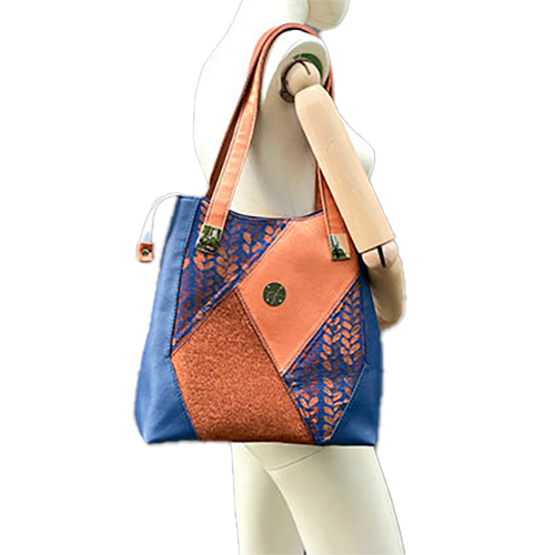 A shoulder bag made up of a patchwork of different materials: royal blue faux leather, golden faux leather, shiny bronze fabric, and blue and bronze wrap fabric with a pattern of small droplets.